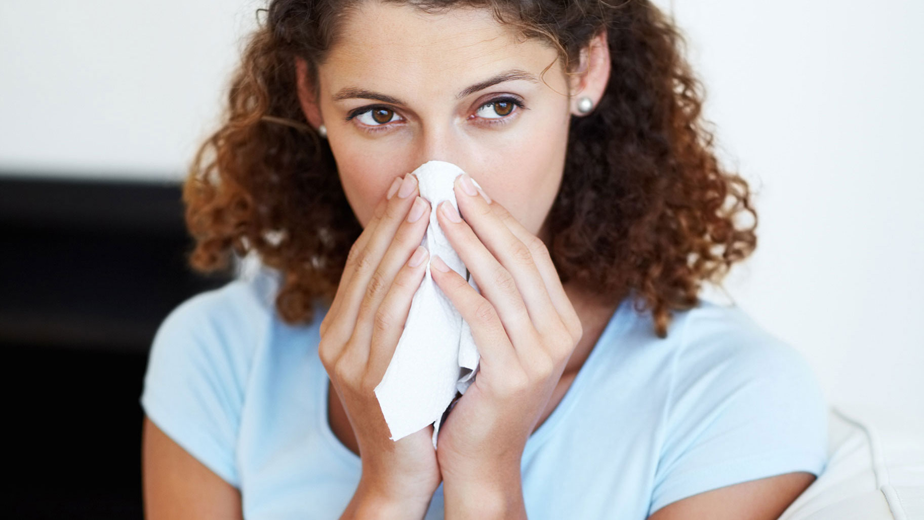 Frau mit Schnupfen durch eine Grippe putzt sich die Nase