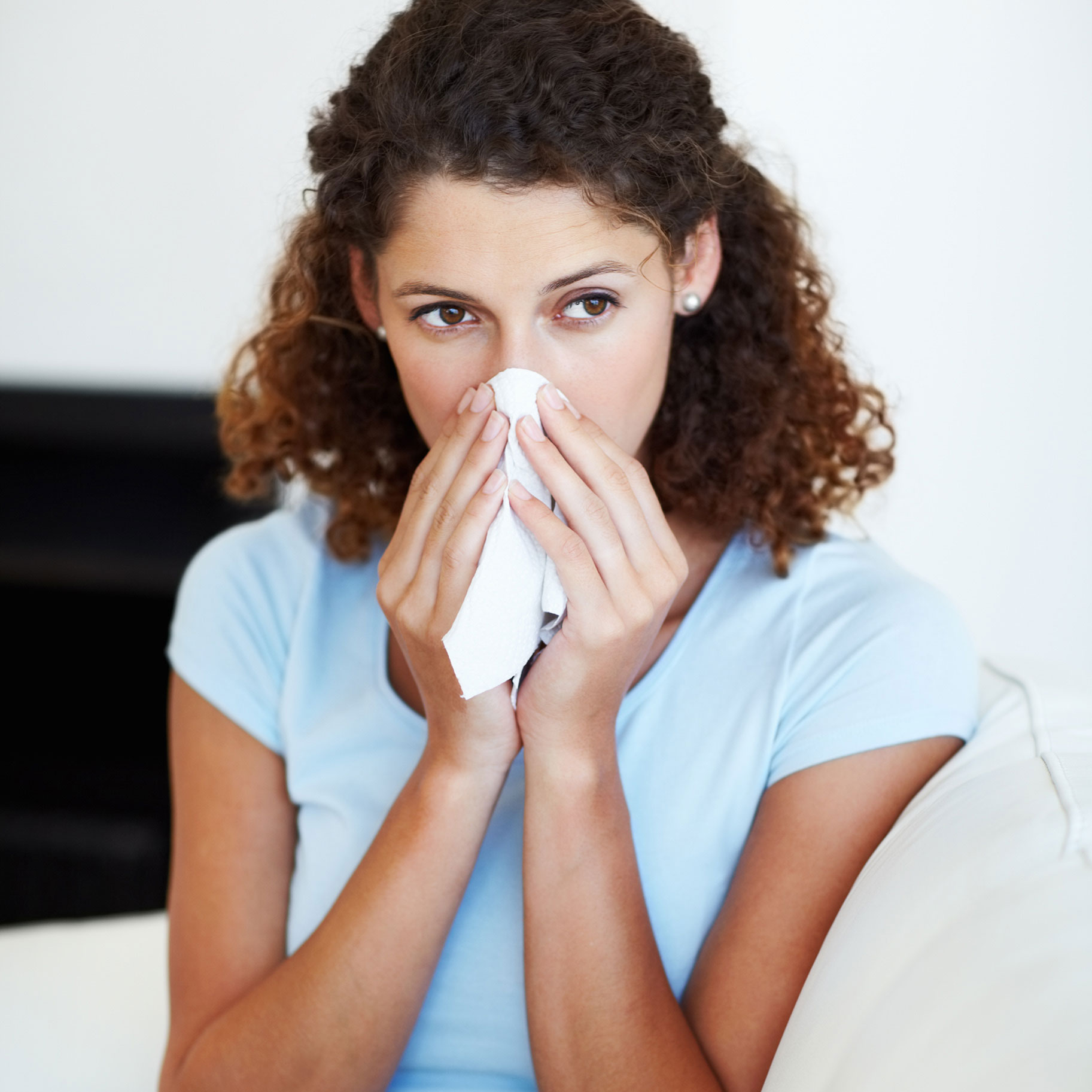 Frau mit Schnupfen durch eine Grippe putzt sich die Nase